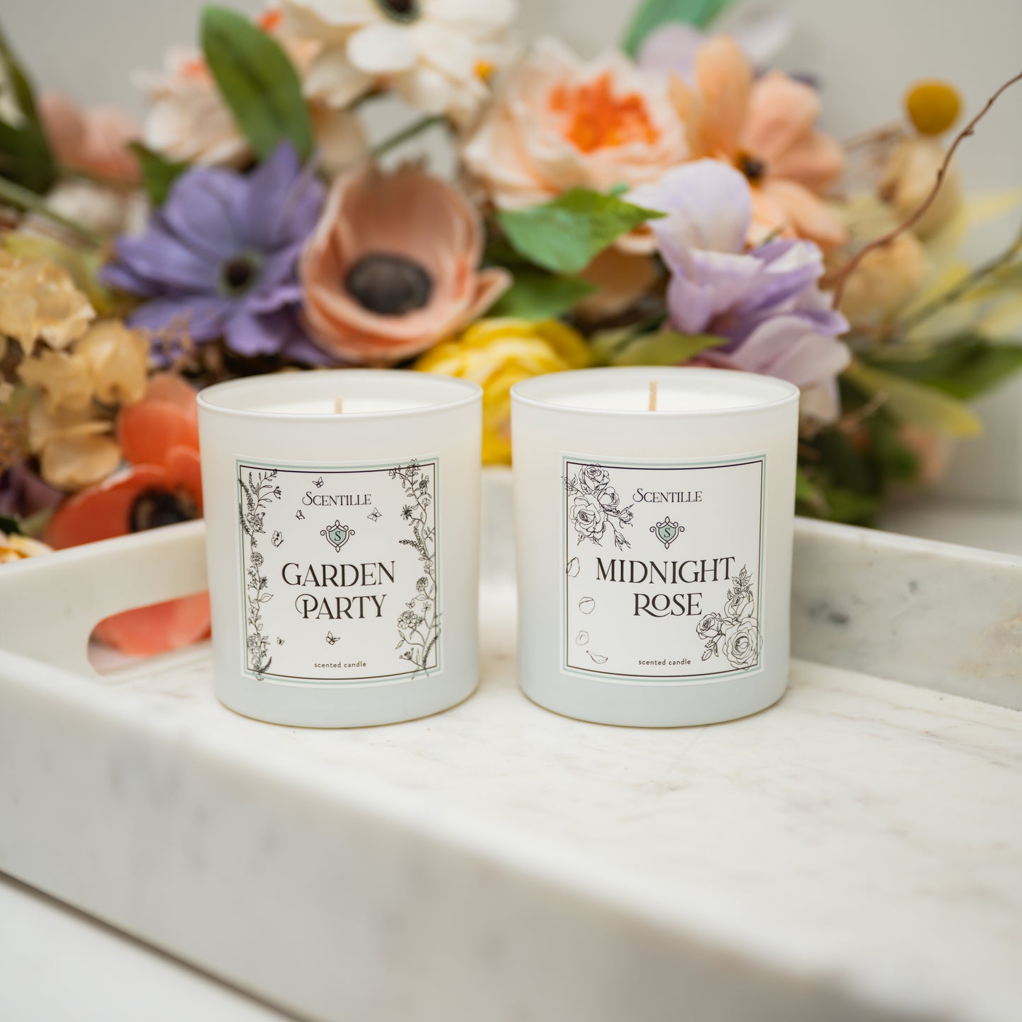 Two candles labeled 'Garden Party' and 'Midnight Rose' on a marble surface with flowers in the background.