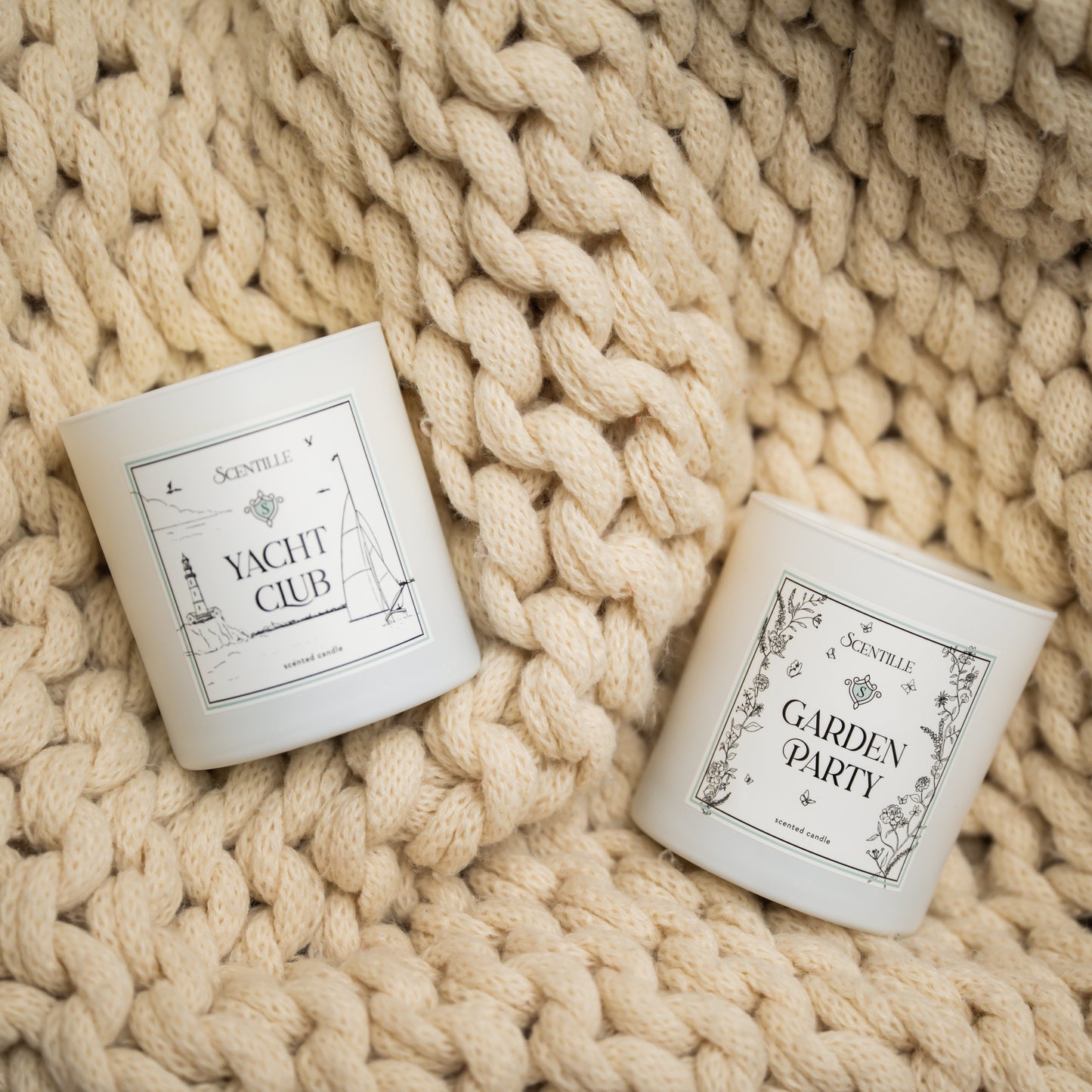Two candles labeled 'Yacht Club' and 'Garden Party' on a textured beige surface.