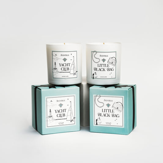 Two candles in boxes labeled 'Yacht Club' and 'Little Black Bag' on a white background