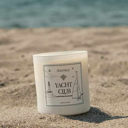 Candle labeled 'Yacht Club' on a sandy beach with ocean in the background