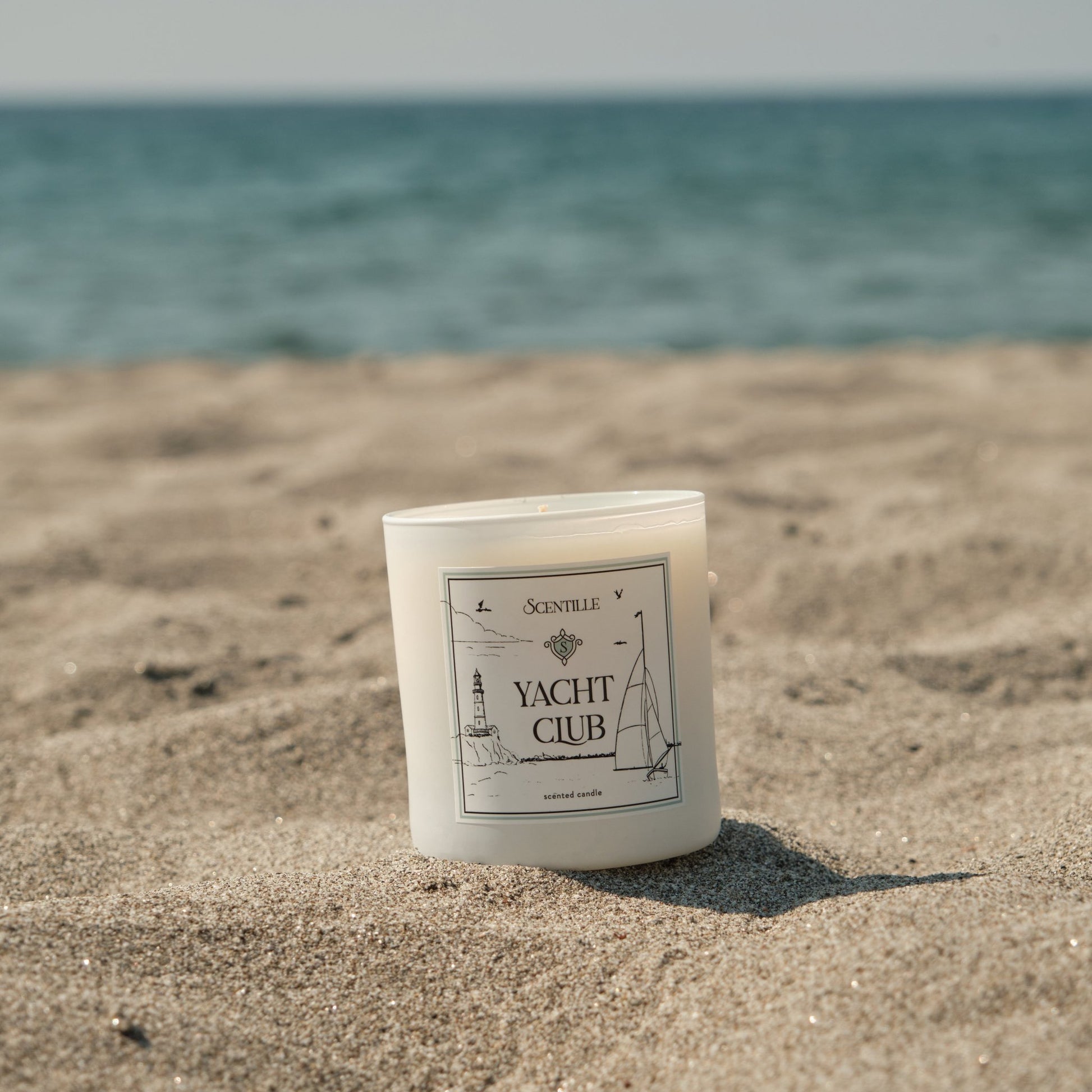 A Yacht Club candle on beach sand