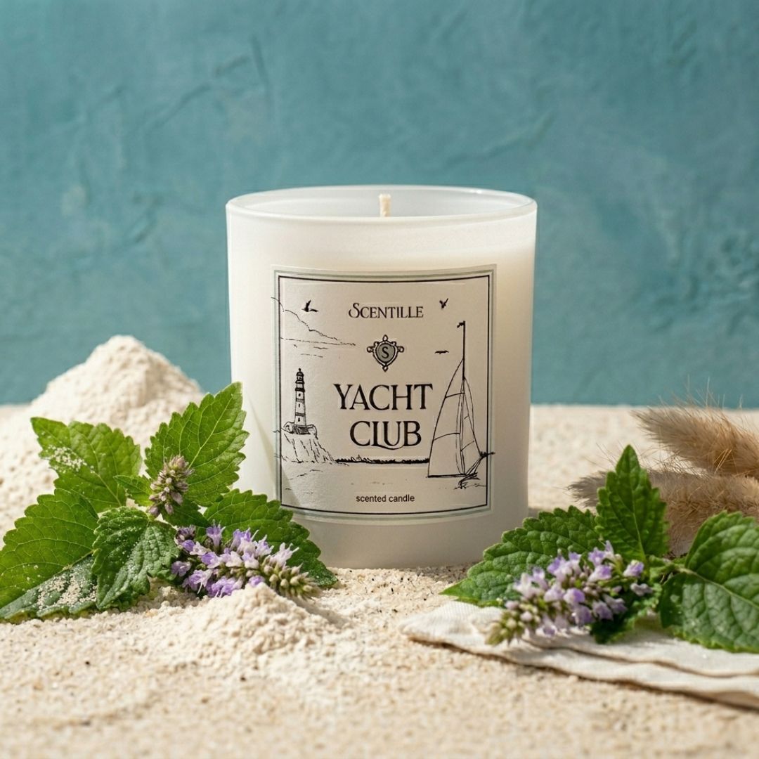 Candle labeled 'Yacht Club' surrounded by sand and greenery on a textured blue background